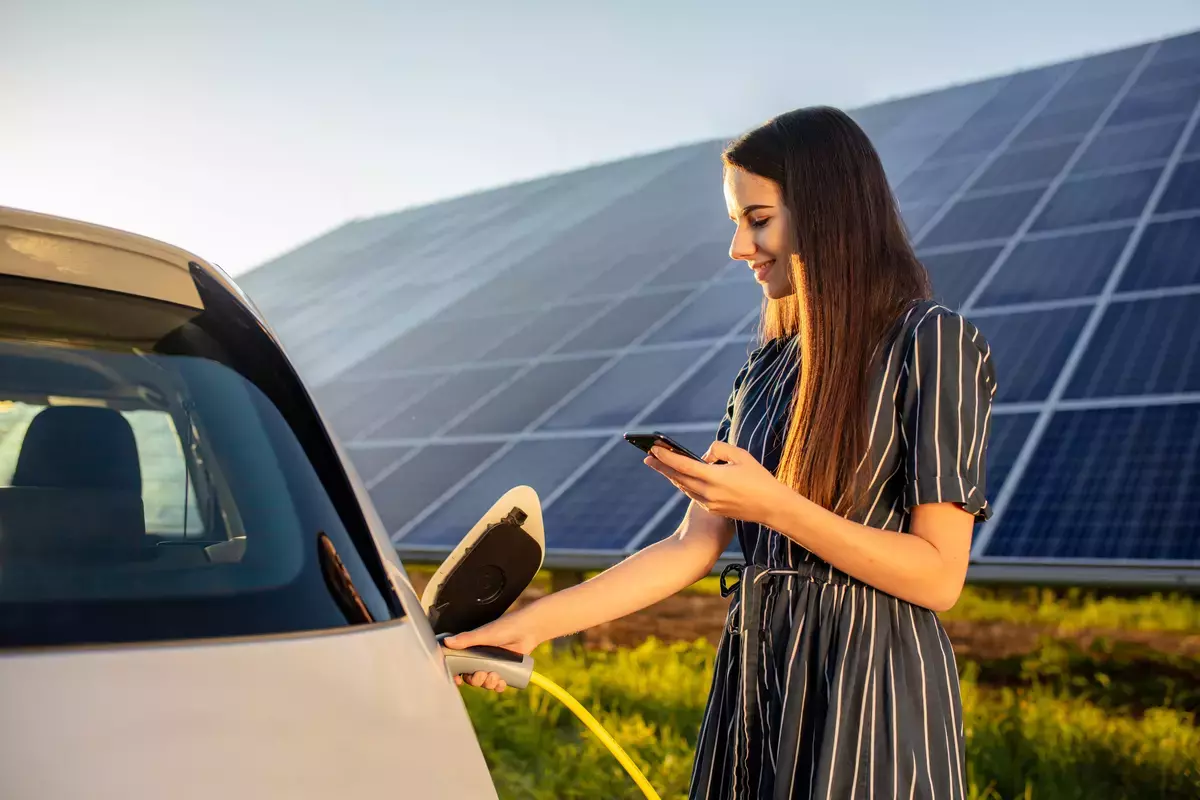 Frau lädt ihr Elektroauto - im Hintergrund eine Solaranlage