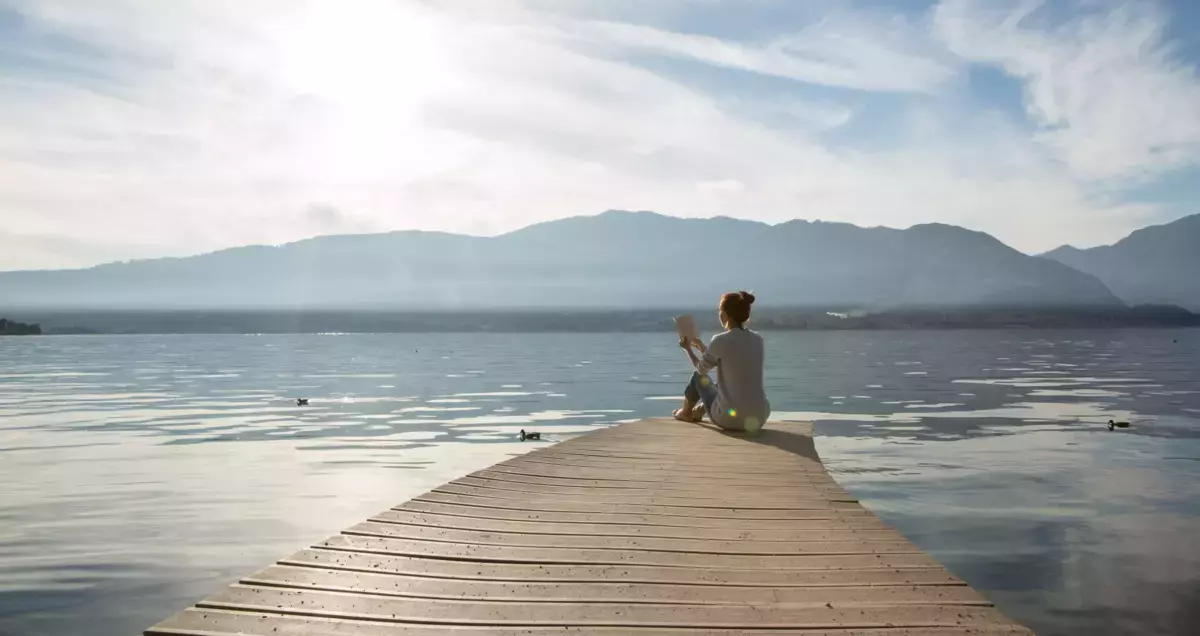 Symbolbild: Junge Frau liest ein Buch an einem italienischen See
